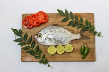 Gerres Fish (Gerres Filamentosus) / Whipfin gümüşi kocakarı Balığı, Tahta bir ped üzerinde köri yaprakları ve domates ile süslenmiş, Beyaz Arkaplan.