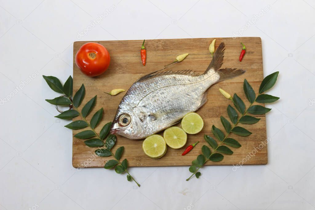 Gerres Fish (Gerres Filamentosus) / Whipfin silver biddy Fish , Decorated with curry Leaves and Tomato on a Wooden pad,White Background.