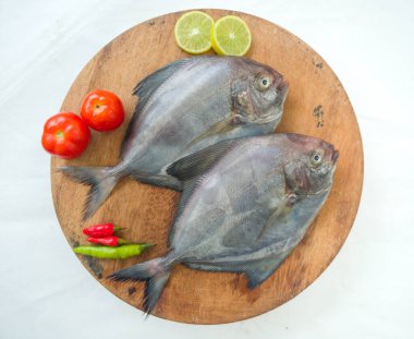 Siyah Pomfret balığının ahşap bir zeminde sebze ve otlarla süslenmiş yakın görüntüsü, Beyaz Arkaplan.
