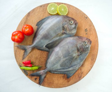 Closeup view of Black Pomfret fish decorated with Vegetables and herbs on a wooden Pad,White Background. clipart