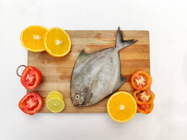 Siyah Pomfret balığının ahşap bir zeminde sebze ve otlarla süslenmiş yakın görüntüsü, Beyaz Arkaplan.