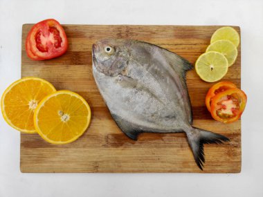 Siyah Pomfret balığının ahşap bir zeminde sebze ve otlarla süslenmiş yakın görüntüsü, Beyaz Arkaplan.