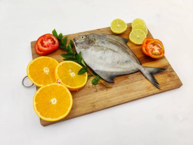 Siyah Pomfret balığının beyaz bir zeminde sebze ve otlarla süslenmiş yakın görüntüsü..