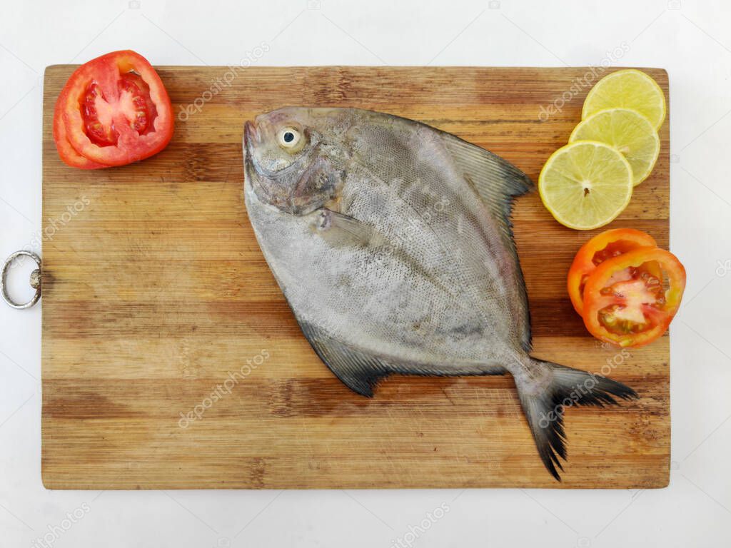 Closeup view of Black Pomfret fish decorated with Vegetables and herbs on a wooden pad,White Background.