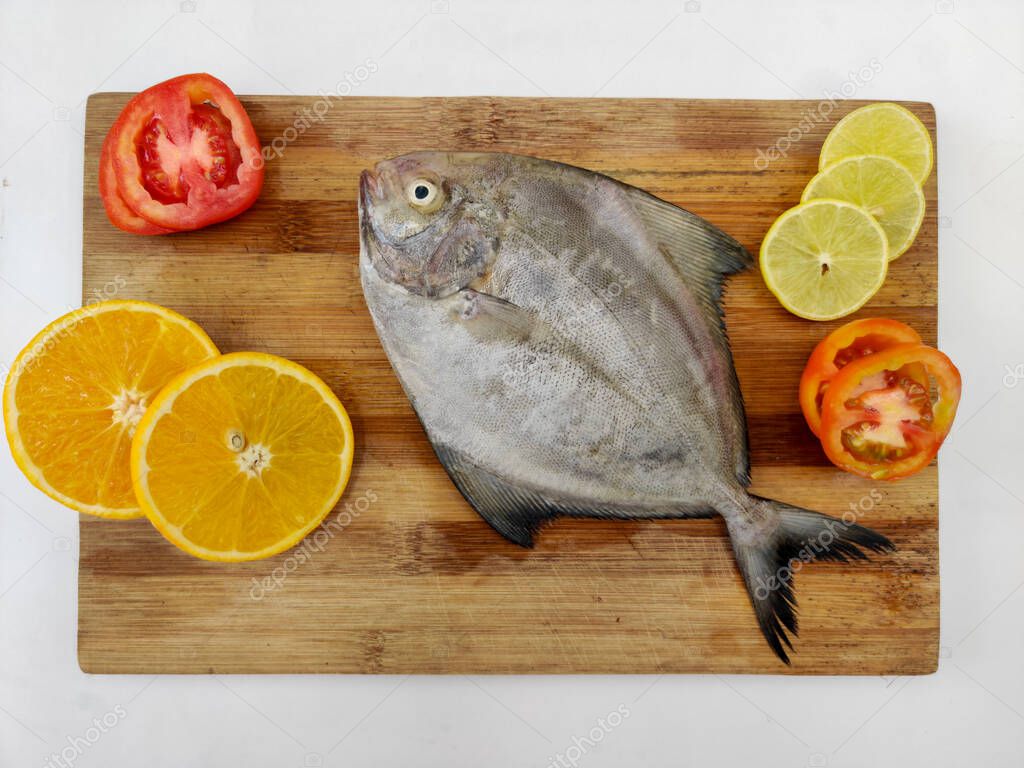 Closeup view of Black Pomfret fish decorated with Vegetables and herbs on a wooden pad,White Background.