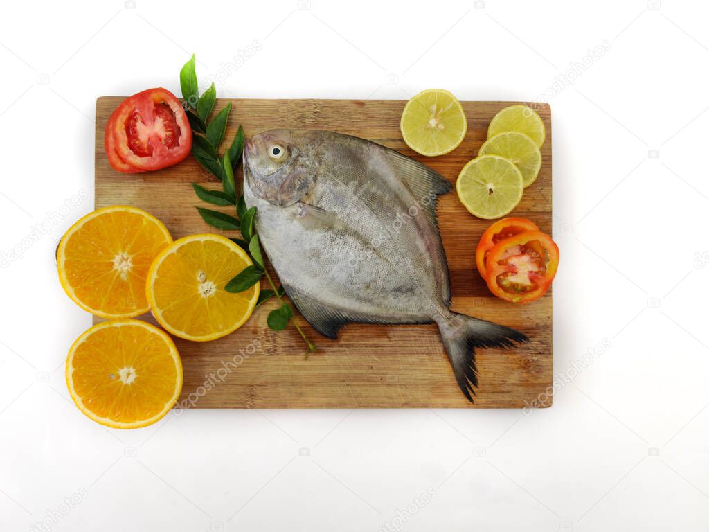 Closeup view of Black Pomfret fish decorated with Vegetables and herbs on a white pad,White Background.