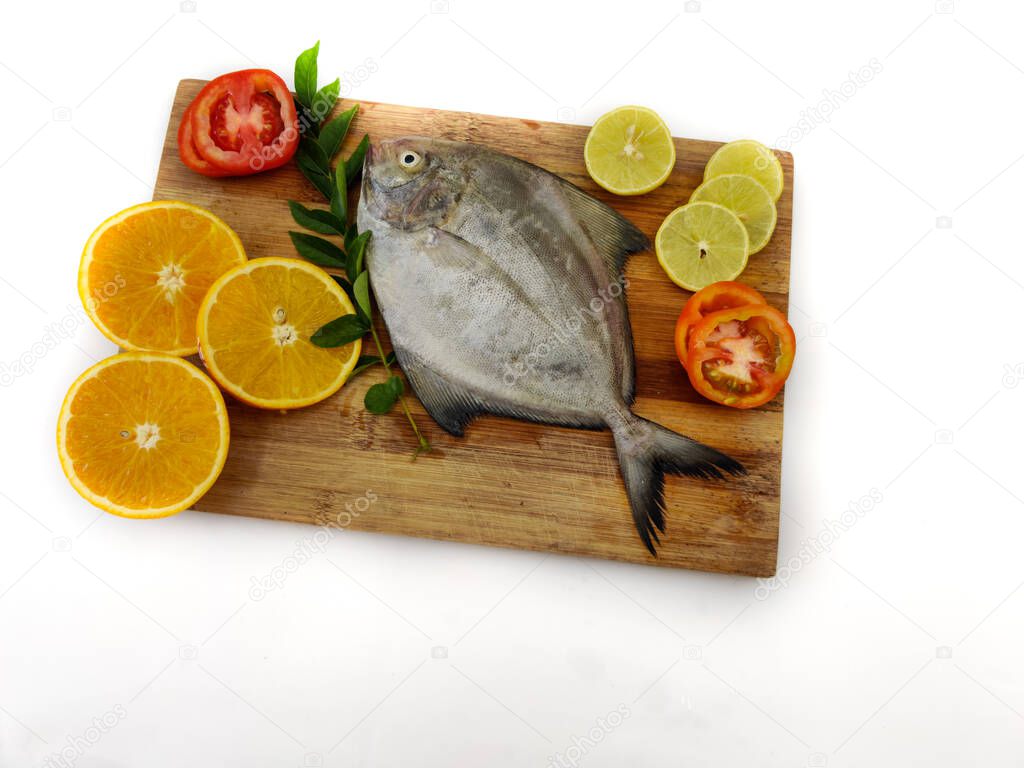 Closeup view of Black Pomfret fish decorated with Vegetables and herbs on a white pad,White Background.