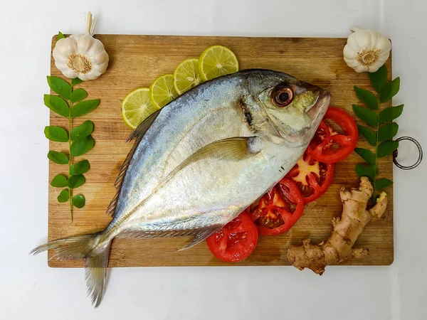Beyaz arka planda köri yaprakları, domates, limon dilimi ve otlarla süslenmiş taze Malabar Trevally Balığının yakın görüntüsü.