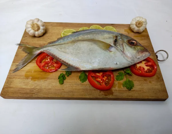 Beyaz arka planda köri yaprakları, domates, limon dilimi ve otlarla süslenmiş taze Malabar Trevally Balığının yakın görüntüsü.