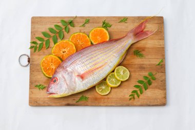Limon dilimi, portakal dilimi ve ahşap bir defter üzerinde köri yapraklarıyla süslenmiş taze Pembe Perch 'in (iplikçik şeklinde) yakın görüntüsü, Beyaz Arkaplan, Seçici odak.