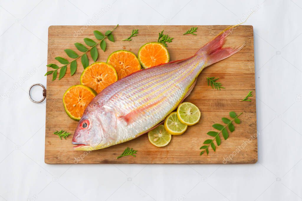 Close up view of fresh Pink Perch (thread finned Bream) Decorated with lemon slice,Orange slice and curry leaves on a wooden pad,White Background,Selective focus.