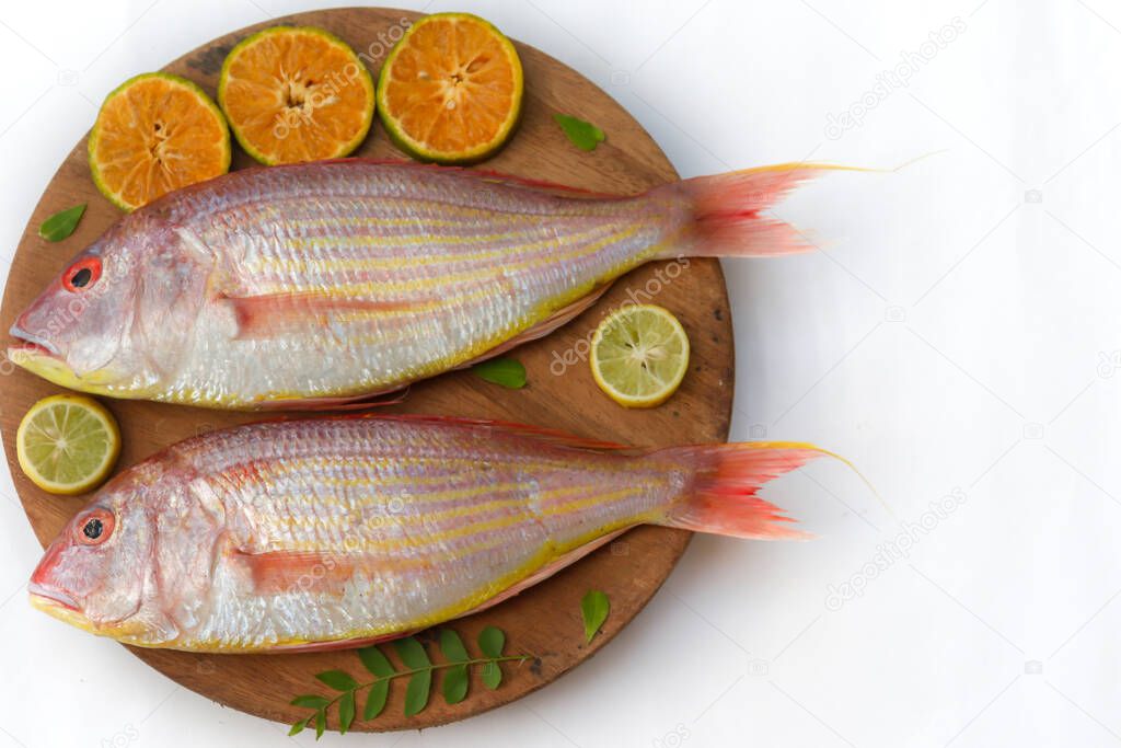 Close up view of fresh Pink Perch (thread finned Bream) Decorated with lemon slice,Orange slice and curry leaves on a wooden pad,White Background,Selective focus.