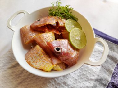 Limon dilimi ve şifalı otlarla süslenmiş yeşil tabakla süslenmiş, temizlenmiş, pembemsi, pembemsi levrek balığını pişirmeye hazır taze manzarayı kapat. Beyaz arka plan, seçici odaklanma..