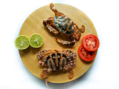 Selective focus of Fresh Crucifix Crab on a wooden pad,Decorated with lemon slice and tomato slice . isolated on a White Background.