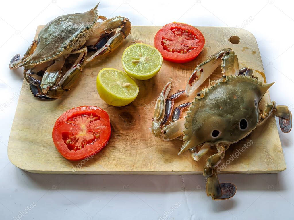 Selective focus of Fresh Three Spotted swimming Crab on a wooden pad,Decorated with lemon slice and tomato slice . isolated on a White Background.