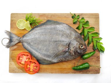 Fresh Black Pomfret Fish decorated with herbs and vegetables on a wooden pad,Selective focus.