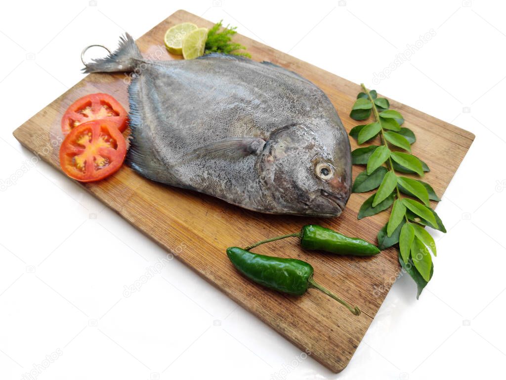 Fresh Black Pomfret Fish decorated with herbs and vegetables on a wooden pad,Selective focus.