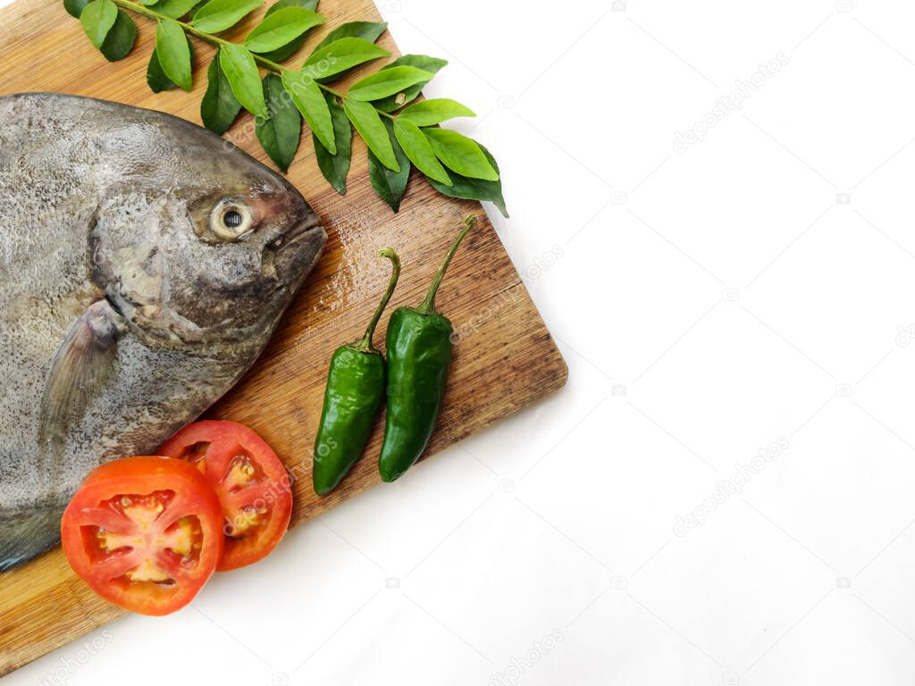 Fresh Black Pomfret Fish decorated with herbs and vegetables on a wooden pad,Selective focus.Space for text.