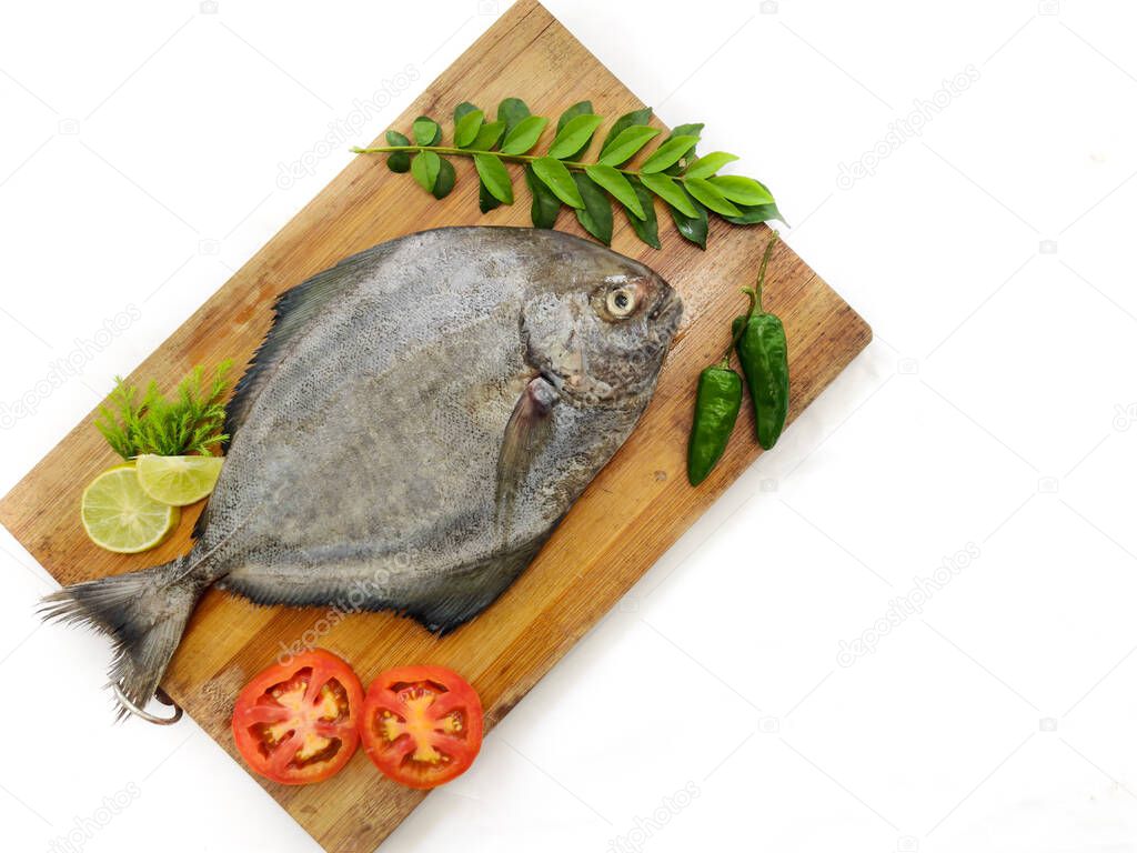Fresh Black Pomfret Fish decorated with herbs and vegetables on a wooden pad,Selective focus.