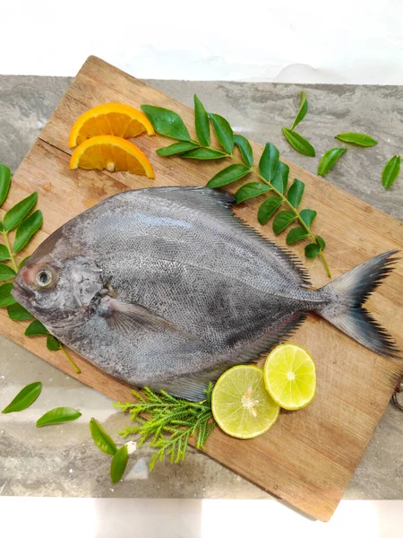 Ahşap bir arka planda meyve ve otlarla süslenmiş siyah pomfret balığının yakın görüntüsü, seçici odaklanma.