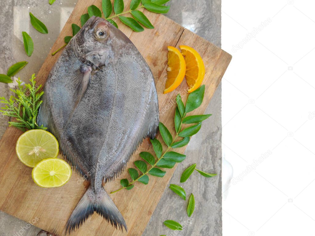 Closeup view of black pomfret fish decorated with fruits and herbs on a wooden background,Selective focus.