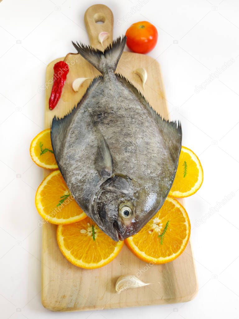 Closeup view of black pomfret fish decorated with fruits and herbs on a wooden pad,white background,Selective focus.