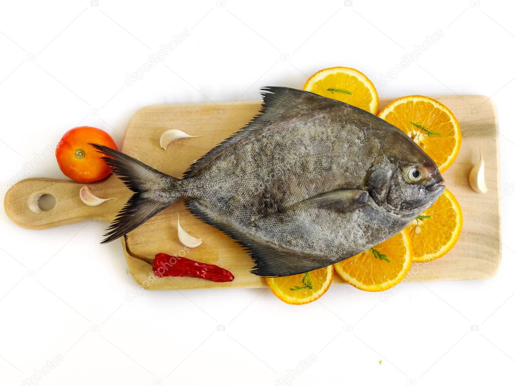 Closeup view of black pomfret fish decorated with fruits and herbs on a wooden pad,white background,Selective focus.