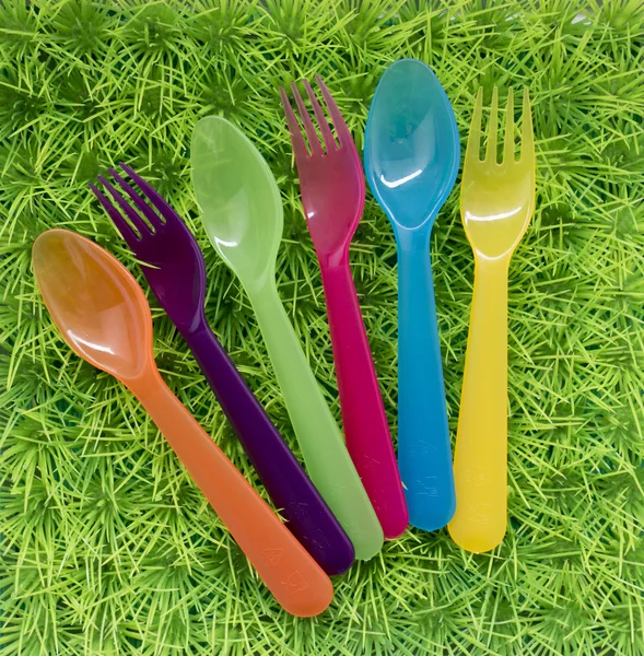 Grön bakgrund med färgade gafflar och skedar för en picknick på — Stockfoto