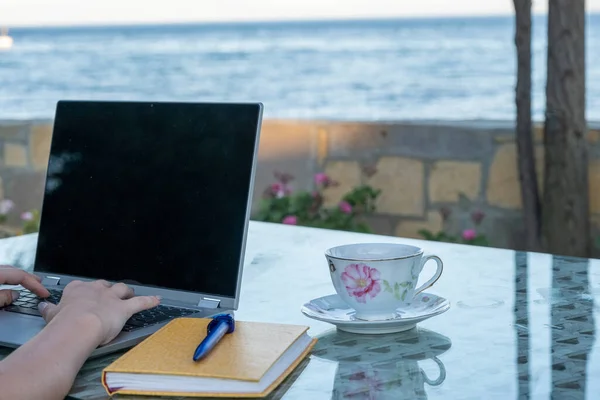 Woman working seaside on laptop and drink coffee, remote professional work life in holiday, home office