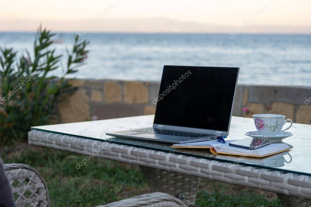 working from summer house remote concept in pandemic, table ready for work with laptop notebook pen phone near the seaside