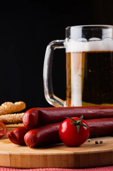 Bicchiere di birra leggera, salsicce di carne e pomodori su tavola di legno — Foto Stock