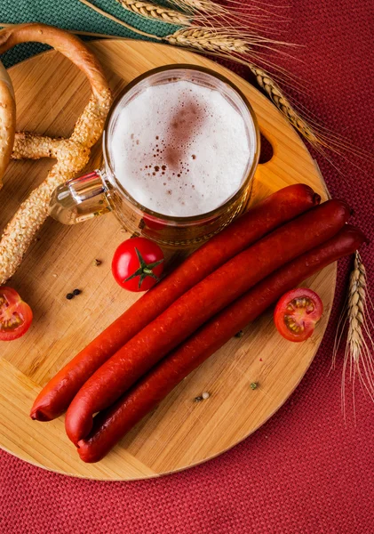 Copo de cerveja leve, salsichas de carne e tomates em tábua de madeira — Fotografia de Stock