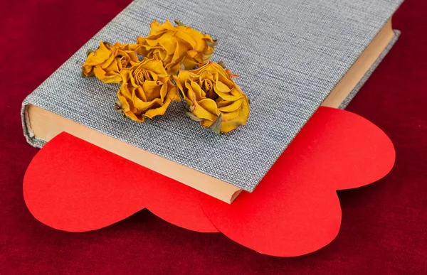 Vier getrocknete gelbe Rosen liegen auf dem Buch mit zwei roten Herzen — Stockfoto