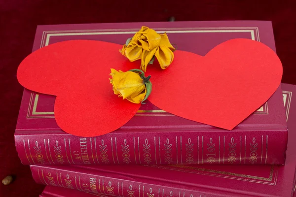 Dwa czerwone serca leży na książki z suszonych róż — Zdjęcie stockowe