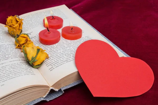 Три красные свечи лежат на книге с бумажным сердцем — стоковое фото