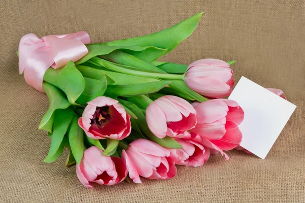 Un ramo de tulipanes rosados con cinta de satén y una pequeña postal — Foto de Stock