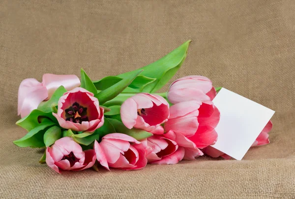 Un ramo de tulipanes rosados con cinta de satén y una pequeña postal — Foto de Stock