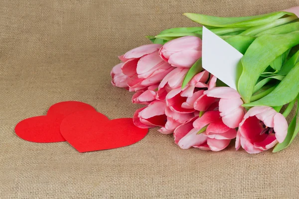 Mehrere rosa Tulpen mit Postkarte und zwei roten Herzen — Stockfoto