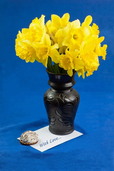 Balde de flores narciso em vaso, envelope sobre fundo azul — Fotografia de Stock