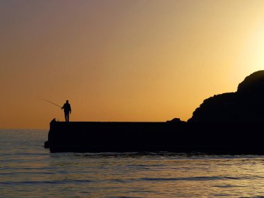 Balearic Adası, Mayorka 'da bir adam gün batımında balık tutuyor.