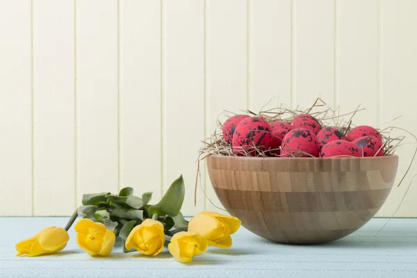 Fundo de Páscoa com ovos vermelhos e tulipas amarelas na parede amarela — Fotografia de Stock