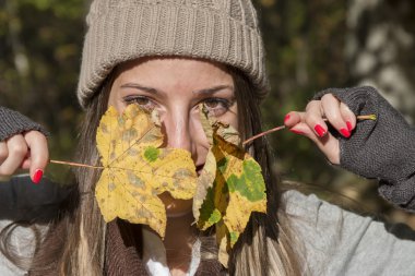 Sonbahar akçaağaç yaprakları ile oynarken şapka ile genç kadın