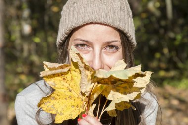 Sonbahar akçaağaç yaprakları ile oynarken şapka ile genç kadın