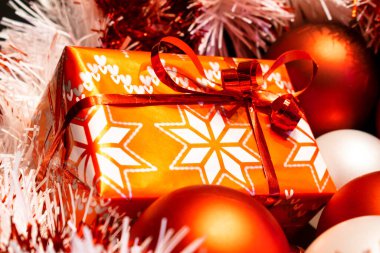 Noel ağacı süslemeleri arasında kırmızı süslemeli kağıda sarılmış Noel hediyesi