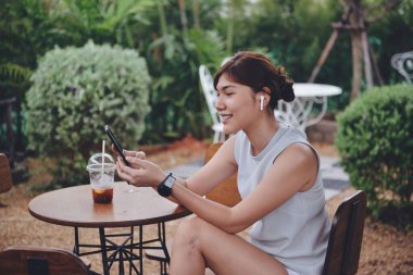 Dijital mobie ve hava kablosuz beyaz kablosuz ile görüntülü sohbet yapan genç bir kadın favori bahçesinde oturup lezzetli bir kahve içerken....