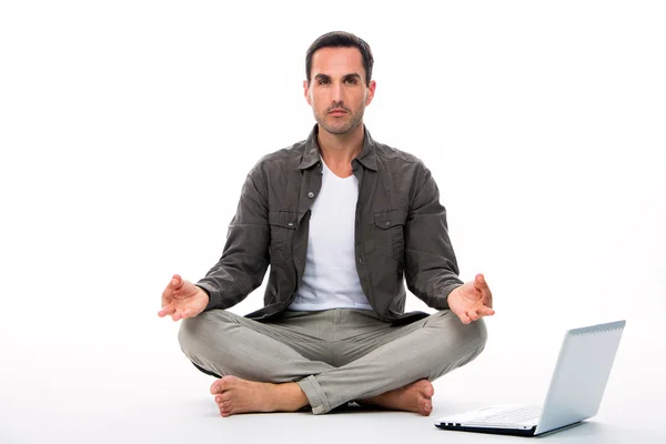 Homme assis sur le sol regardant la caméra et pratiquant le yoga avec ordinateur portable à côté de lui — Photo