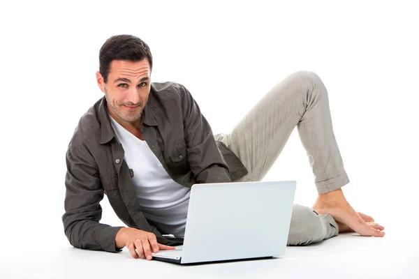 Man laying on the floor, smiling at camera and working with his laptop — Stock Photo, Image