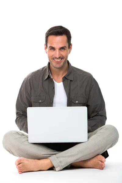 Homem sentado no chão, sorrindo para a câmera e trabalhando com seu laptop — Fotografia de Stock