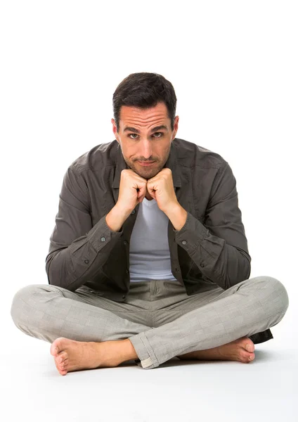 Pensativo hombre sentado en el suelo, mirando a la cámara, con las manos bajo la barbilla —  Fotos de Stock