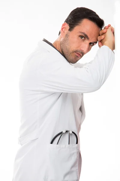 Retrato de perfil de medio cuerpo de un médico varón reflexivo, mirando a la cámara, con las manos apoyadas en una pared — Foto de Stock